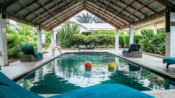 A covered swimming pool with lounge chairs and a slide.