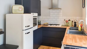 Una cocina compacta con un refrigerador blanco, un horno integrado, una estufa a gas y una encimera de madera.
