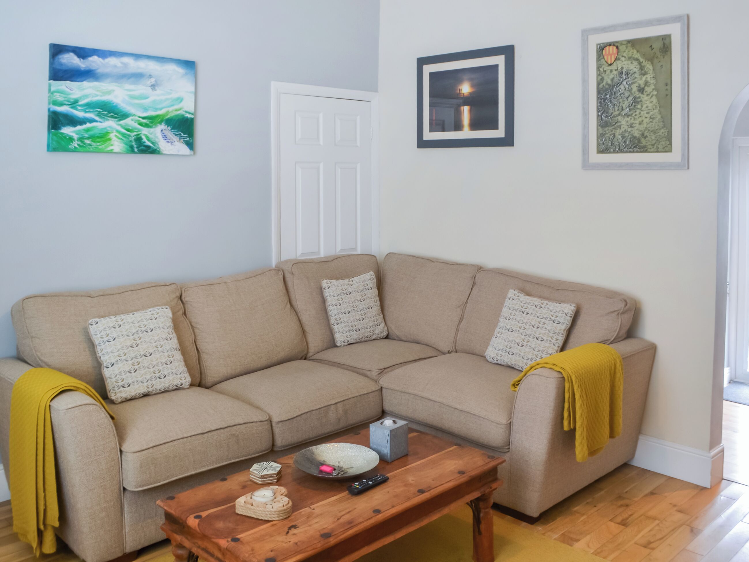 A living room with a beige sectional sofa, a wooden coffee table, and three framed artworks on the wall.