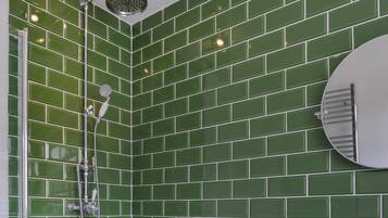 Une douche d’angle avec des carreaux verts, un miroir rond et un pommeau de douche.