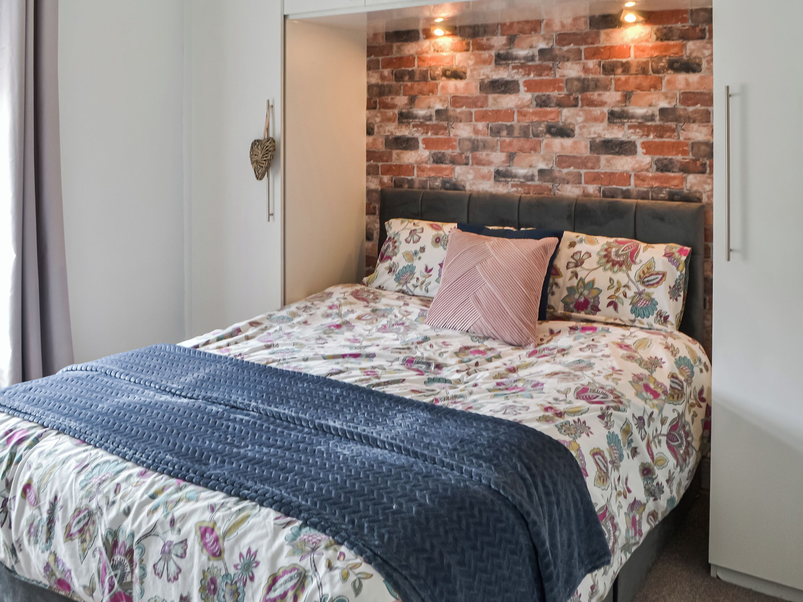 Un dormitorio con pared de ladrillo, ropa de cama floral y cabecera.