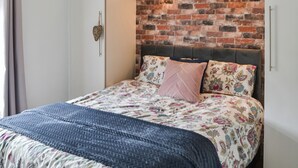 Un dormitorio con pared de ladrillo, ropa de cama floral y cabecera.