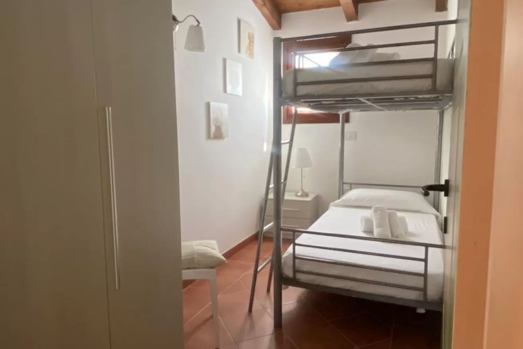 A bunk bed room with a ladder, a bedside table, and a lamp.