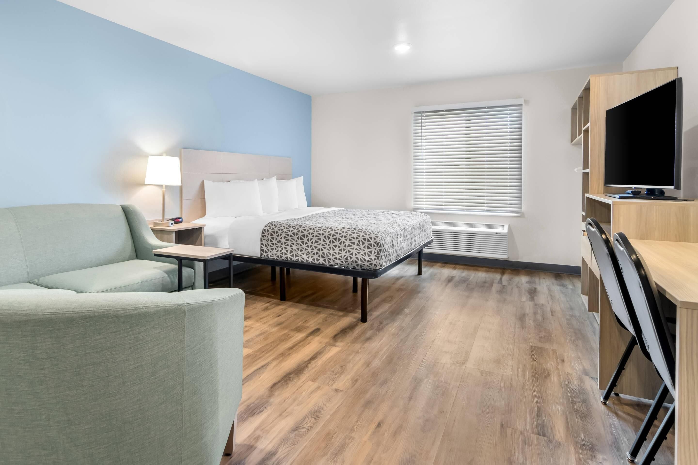 A hotel room with a bed, a desk, a chair, a TV, and a window with blinds.