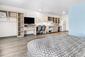 Ein modernes Hotelzimmer mit Bett, Schreibtisch, Stuhl, Fernseher und einer Küchenzeile.