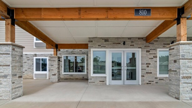 A building entrance with stone walls, wooden beams, and a number sign '810'. - Woodspring Suites Elkhart (Elkhart)