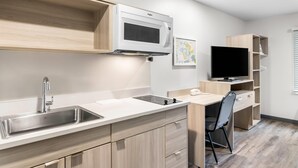 A compact kitchen with a microwave, sink, and wooden cabinets. - Woodspring Suites Elkhart (Elkhart)