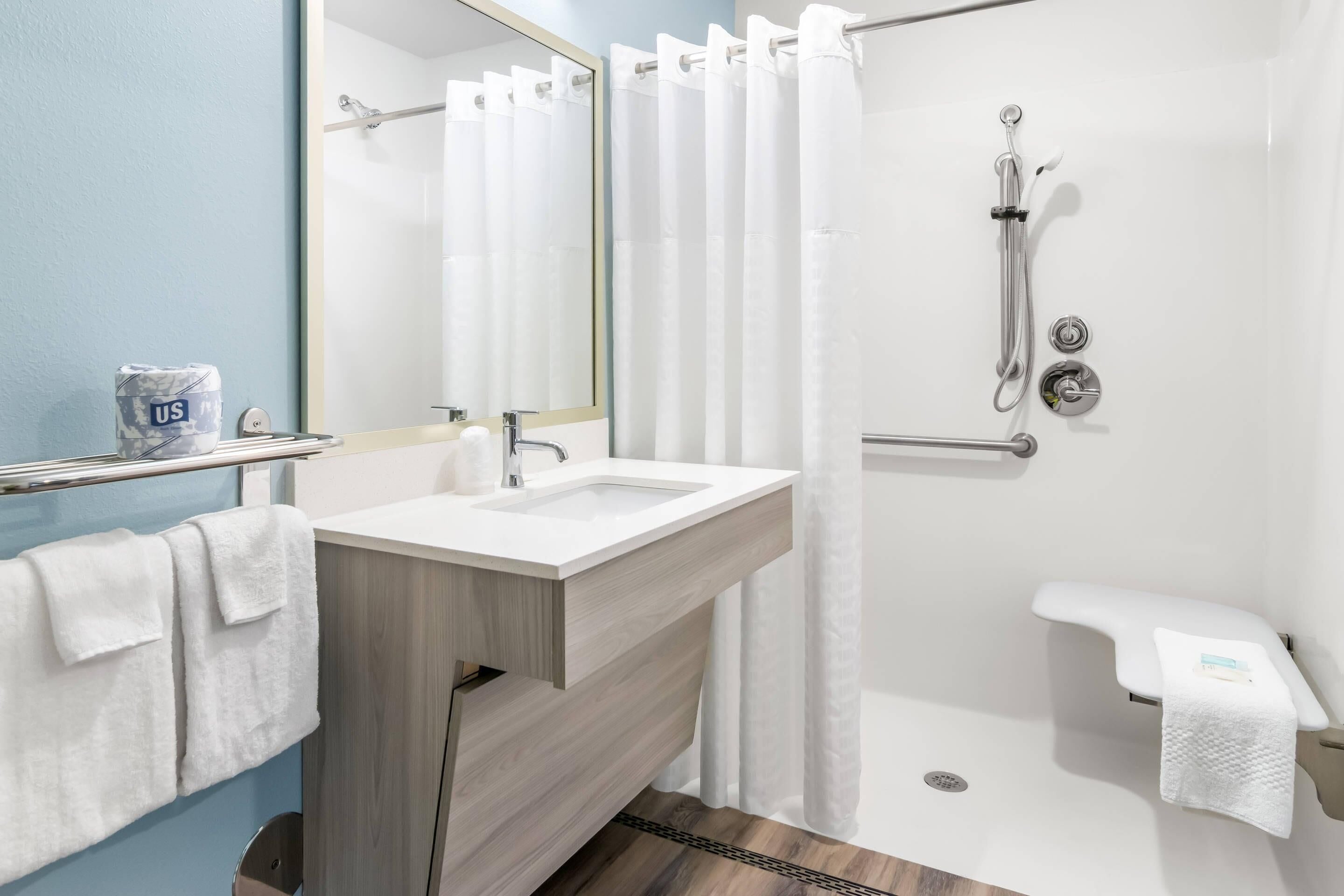 Ein modernes Badezimmer mit Waschbecken, Spiegel, Dusche und Handtuchhalter.