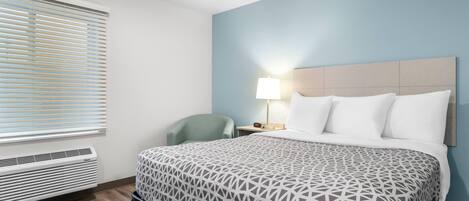 A hotel room with a bed, a nightstand, a lamp, a chair, and a window with blinds.