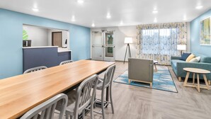 A modern, well-lit room with a wooden dining table, grey chairs, a grey sofa, and a blue accent wall. - Woodspring Suites Elkhart (Elkhart)