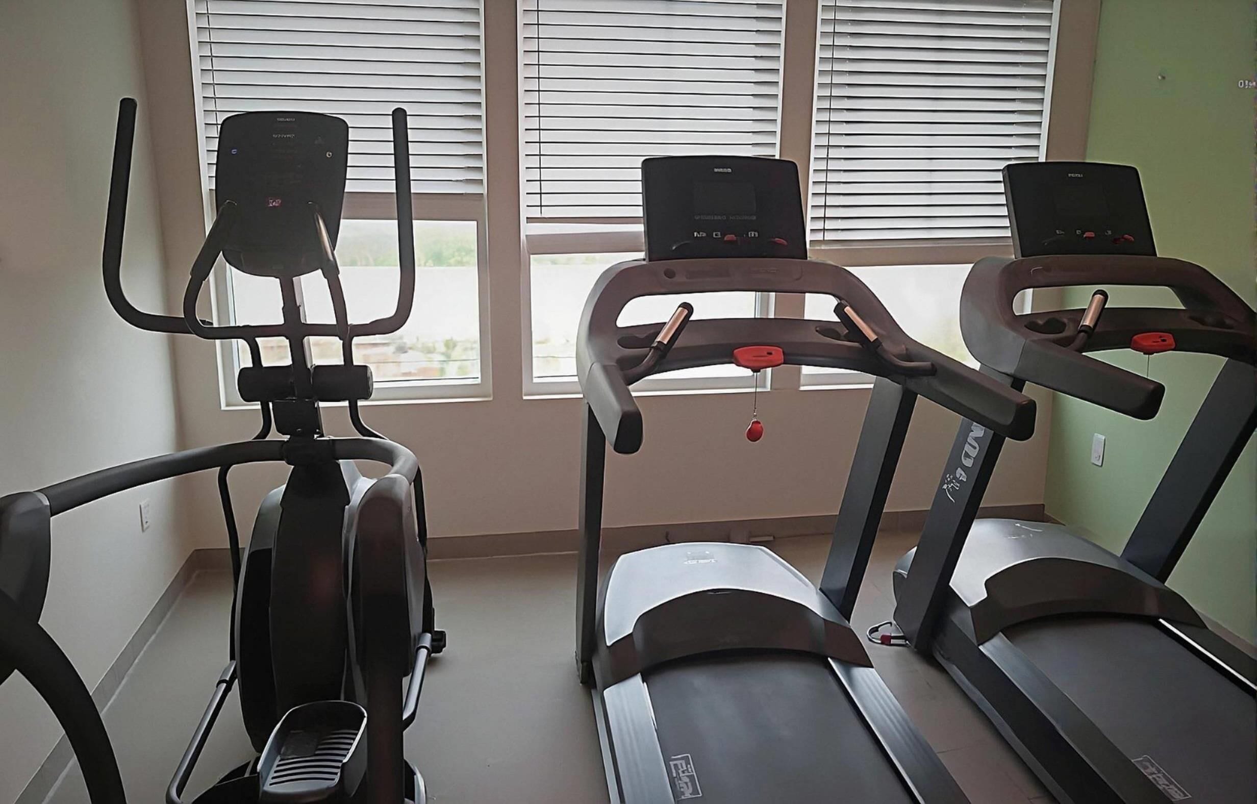Une salle de sport équipée de trois tapis de course et d’un appareil elliptique.