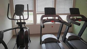 Une salle de sport équipée de trois tapis de course et d’un appareil elliptique.
