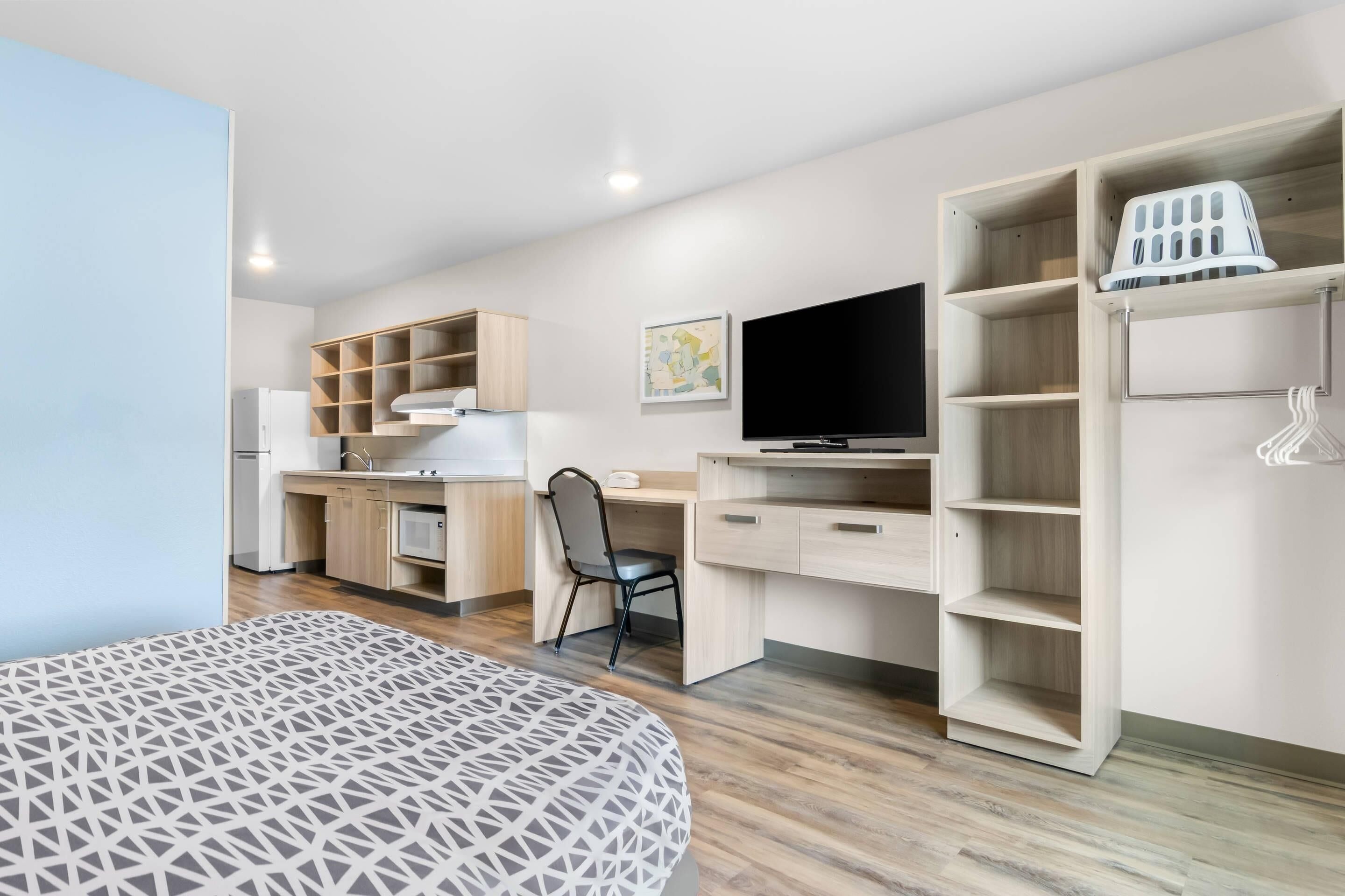 A modern bedroom with a bed, a desk, a chair, a TV, and built-in shelving.