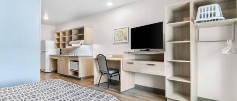 A modern bedroom with a bed, a desk, a chair, a TV, and built-in shelving.