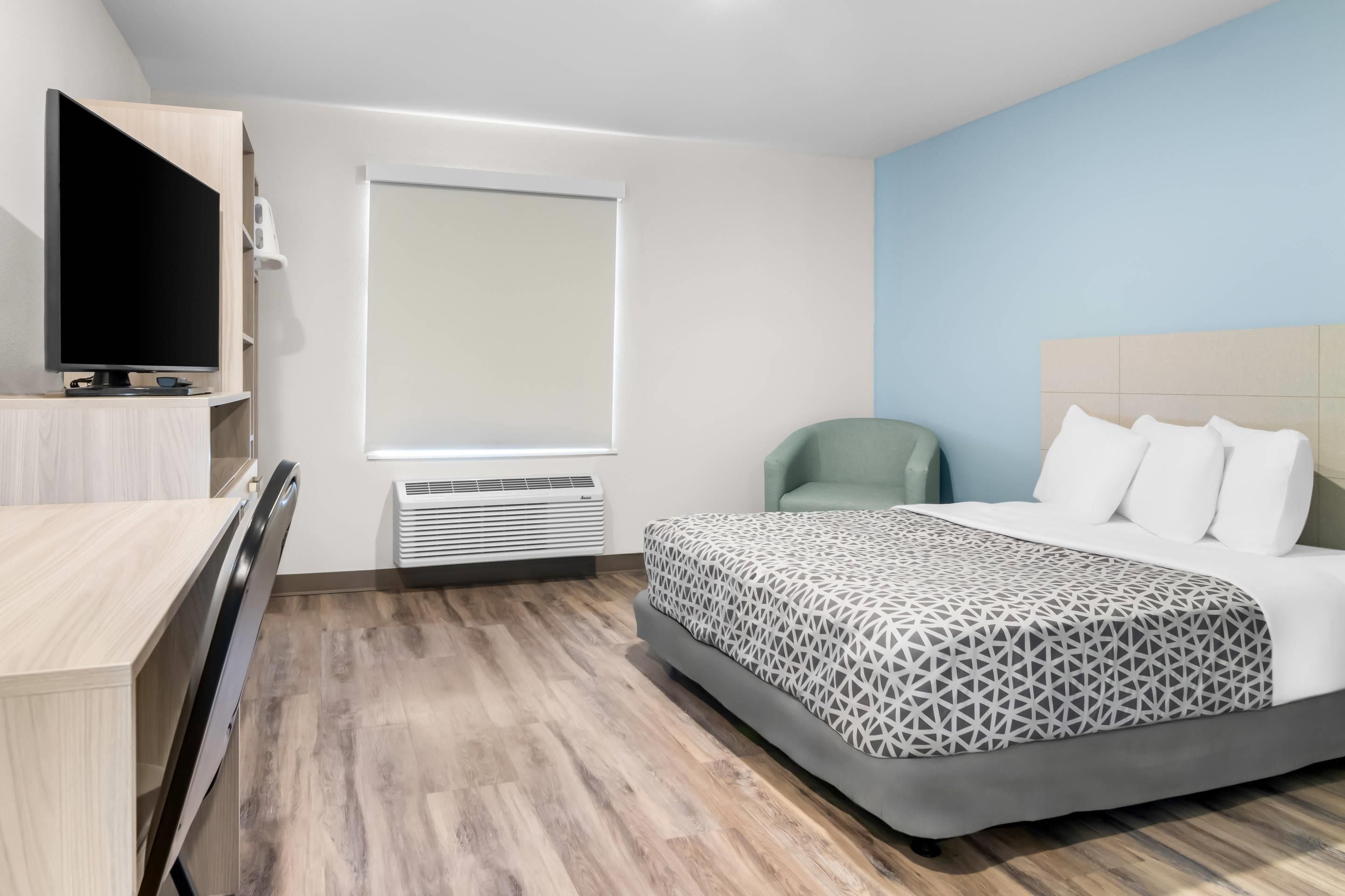 A hotel room with a bed, a television, a window, and a chair.