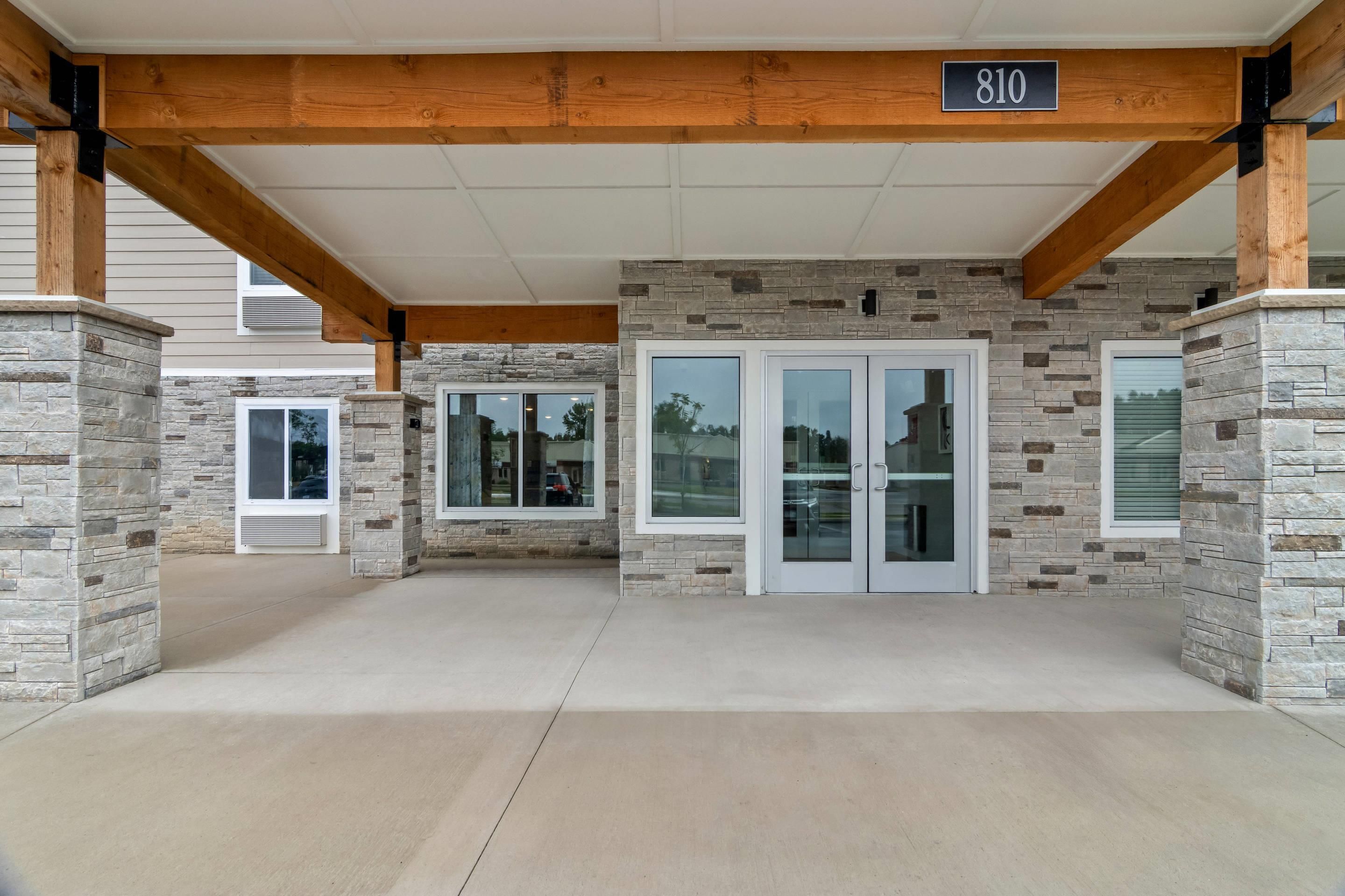 A building entrance with stone walls, a wooden beam structure, and a number sign indicating the address.