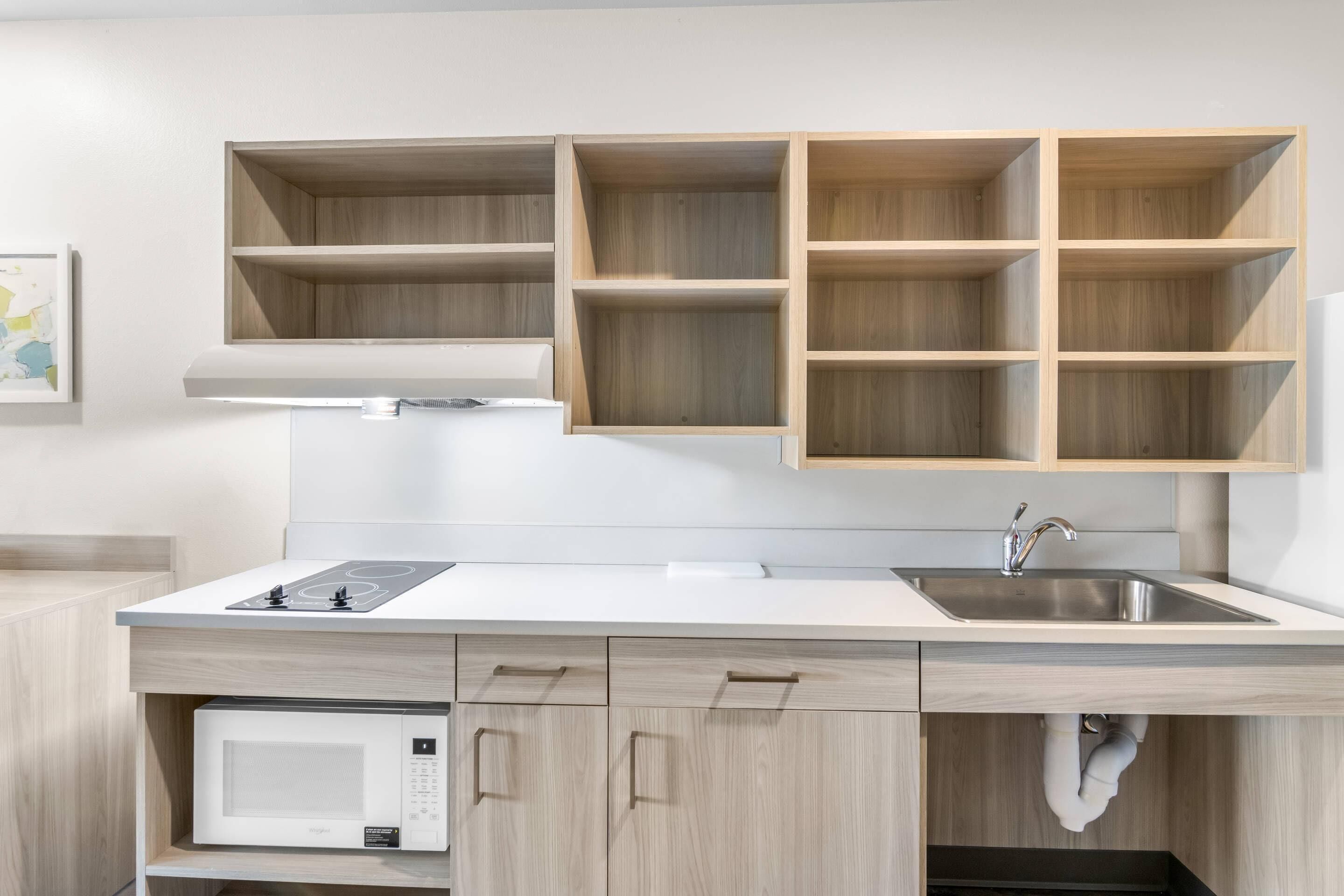 A modern kitchen with wooden cabinets, a white countertop, a built-in microwave, and a stainless steel sink.