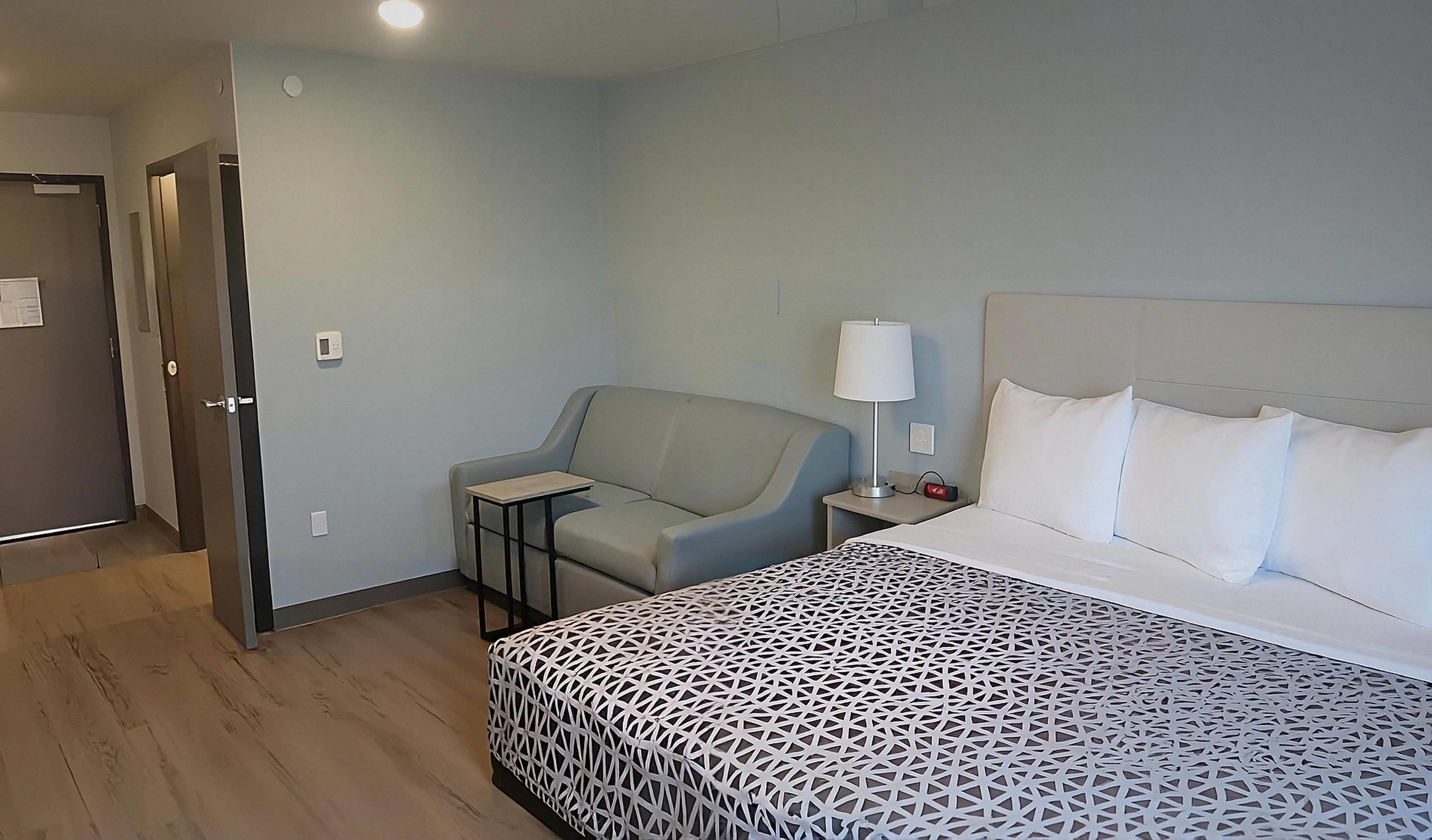 Una habitación de hotel con una cama, una silla, una mesita de noche, una lámpara y una puerta.