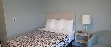 Una cama bien hecha con una colcha estampada, una mesita de noche con una lámpara y una silla en una habitación con paredes azul claro.