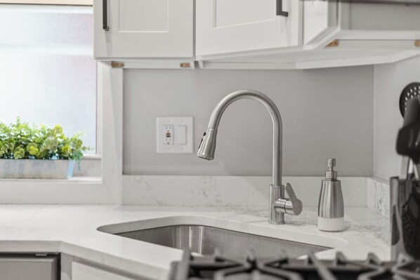A modern kitchen with white cabinets, a stainless steel sink, and a gas stove.