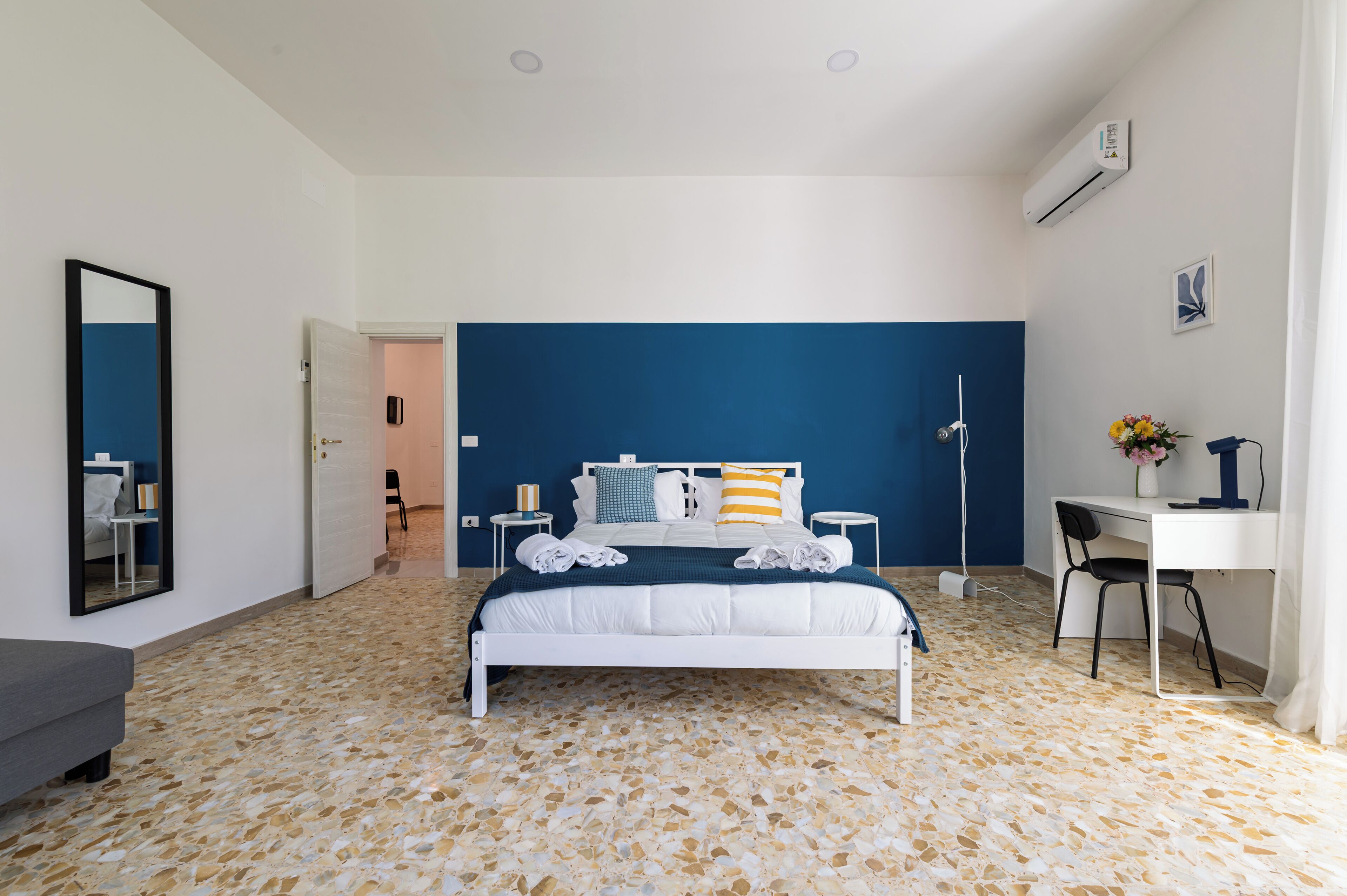 Une chambre à coucher avec un lit, un bureau, une chaise, un miroir et une porte.