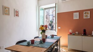 A dining area with a wooden table, chairs, a vase with flowers, and a window with a view of buildings. - Casa Luce del Sole - Two Bedroom Apartment, Sleeps 5 (Naples)