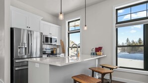 Une cuisine moderne dotée d’appareils électroménagers en acier inoxydable, d’un plan de travail blanc et de tabourets en bois.