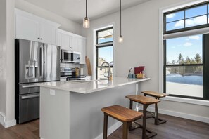 A modern kitchen with stainless steel appliances, a white countertop, and wooden stools. - New Egg Harbor Construction with Pool,Hot Tub,Gym (Egg Harbor)