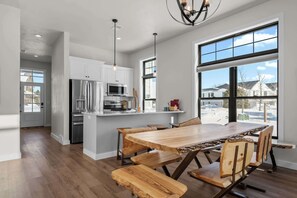 A modern kitchen with stainless steel appliances, a wooden dining table, and large windows. - New Egg Harbor Construction with Pool,Hot Tub,Gym (Egg Harbor)
