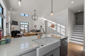 A modern kitchen with a large island, a dining area with a sofa and chairs, and a staircase leading to another level. - New Egg Harbor Construction with Pool,Hot Tub,Gym (Egg Harbor)