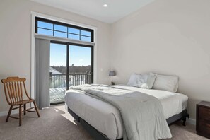 A bedroom with a large window, a bed, a chair, and a nightstand.