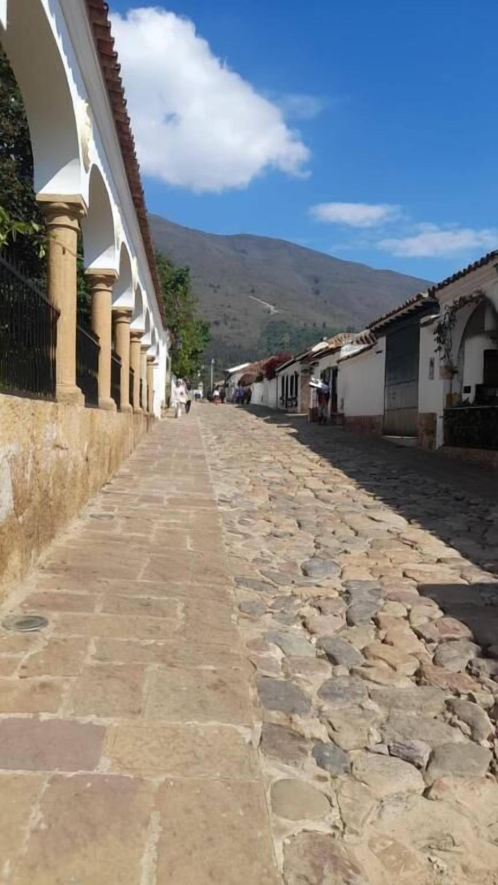 Una calle empedrada bordeada de edificios tradicionales, algunos con arcos y techos de tejas, que conduce hacia una montaña al fondo.