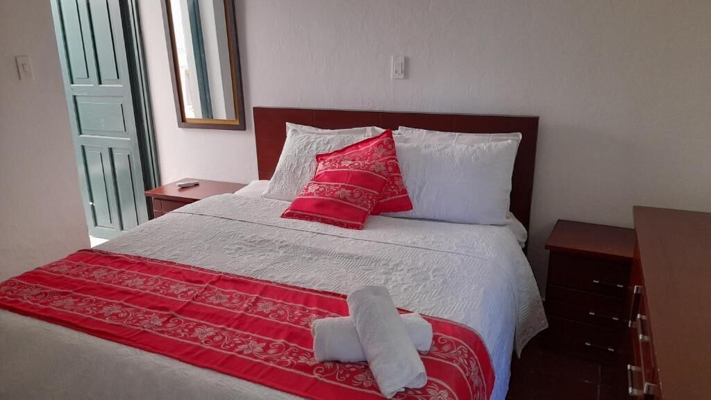 Un lit bien fait, avec une literie blanche et rouge, un plaid à motifs rouges et blancs, et une paire de serviettes blanches.