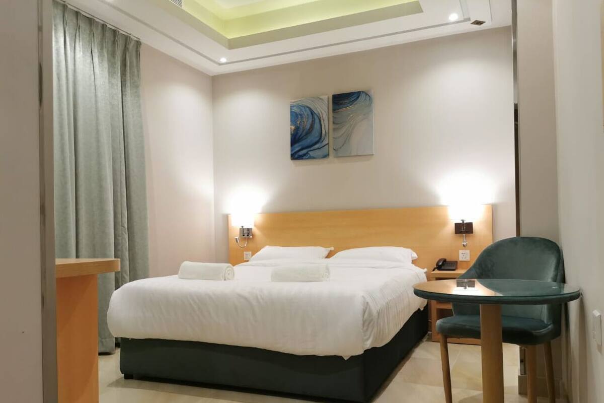 A hotel room with a bed, a desk, a chair, and two wall-mounted lamps.