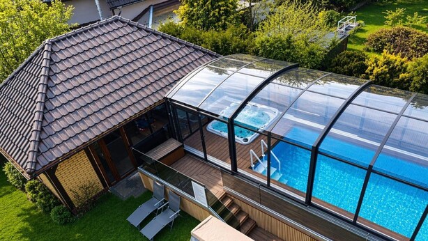 Una piscina cubierta con vidrio, tinas de hidromasaje, una terraza de madera y un pequeño pabellón.