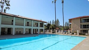 A swimming pool with clear blue water, surrounded by a building with multiple balconies and a tiled roof. - 2-Bedroom Condo - close to all! (San Diego)