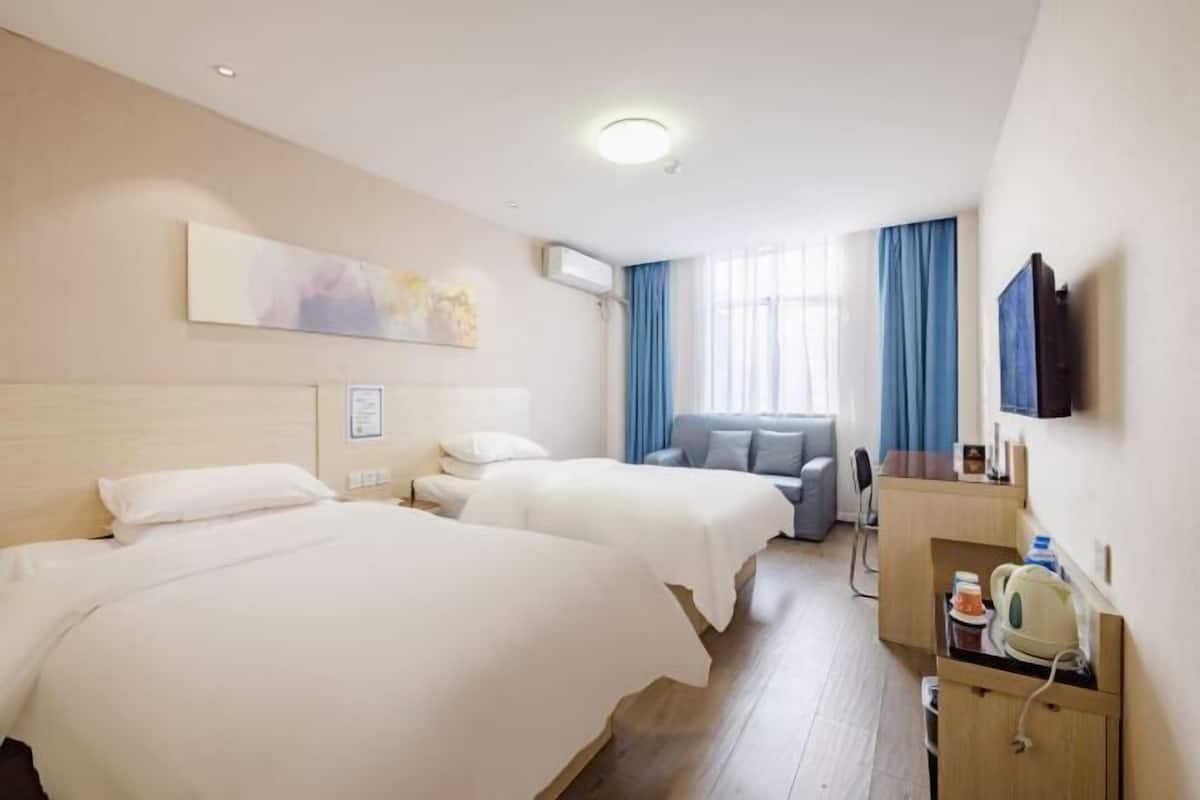 Quarto de hotel com duas camas, uma escrivaninha, televisão e janela com cortinas.
