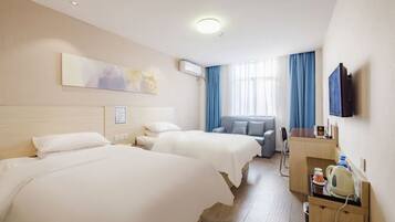 Habitación de hotel con dos camas, un escritorio, televisor y ventana con cortinas.