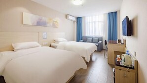 Ein Hotelzimmer mit zwei Betten, einem Schreibtisch mit Wasserkocher, einem Flachbildfernseher und einem Fenster mit blauen Vorhängen.