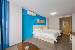 Ein Hotelzimmer mit Bett, Schreibtisch, Stuhl, blauer Wand und Klimaanlage.