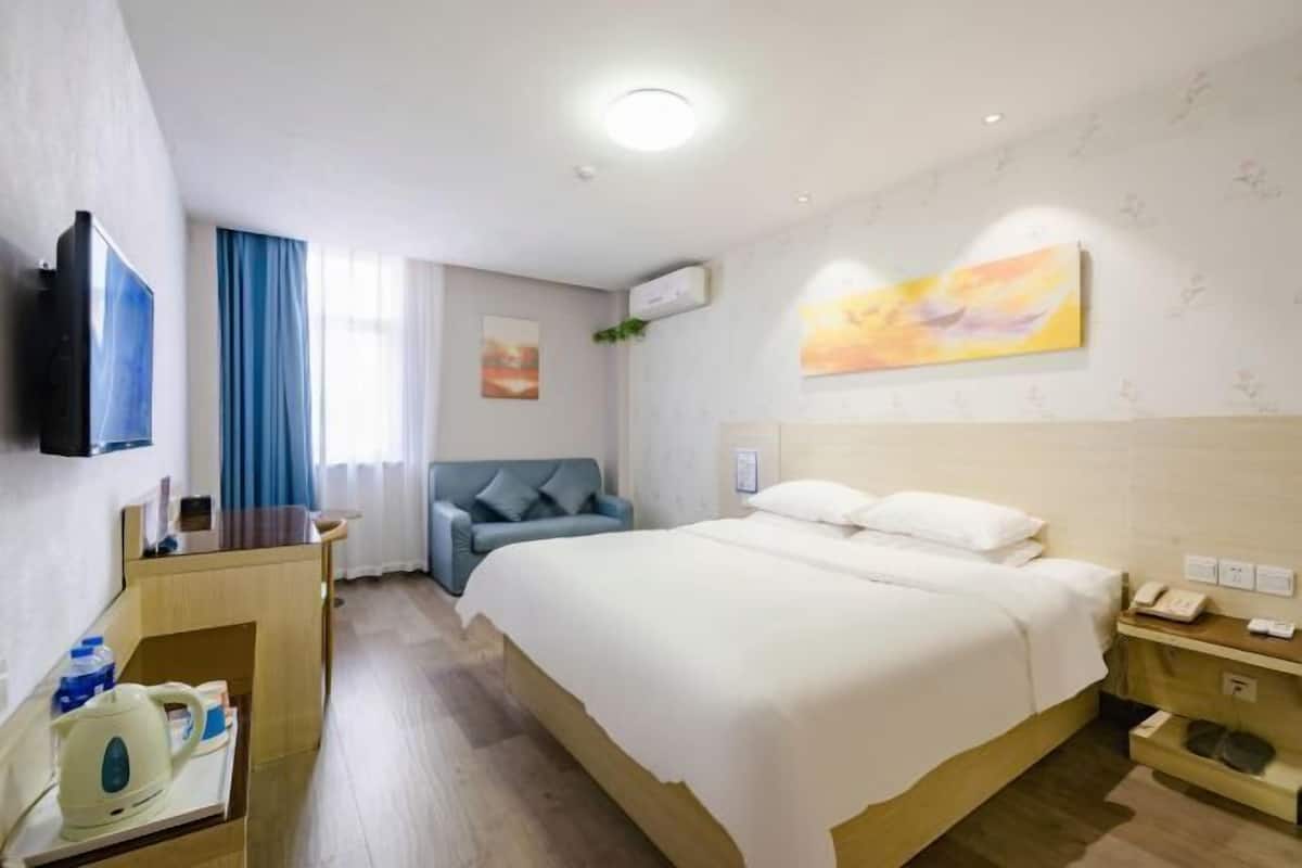 Quarto de hotel com cama, televisão, secretária com chaleira e janela com cortinas.