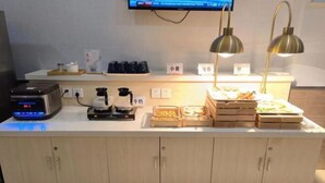 Un buffet proposant une variété de plats, une machine à café et un téléviseur fixé au mur.