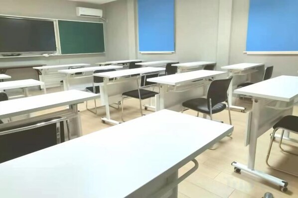 Un aula con pupitres y sillas dispuestos en filas, una pizarra y una pantalla para proyector.