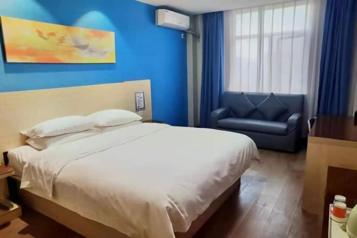 Quarto de hotel com cama, sofá, um quadro na parede e janela com cortinas.