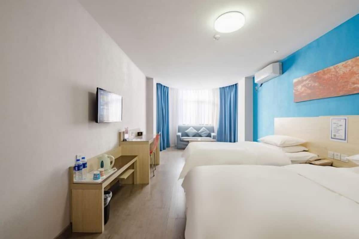 Quarto de hotel com cama, escrivaninha, cadeira, televisão e janela com cortinas.