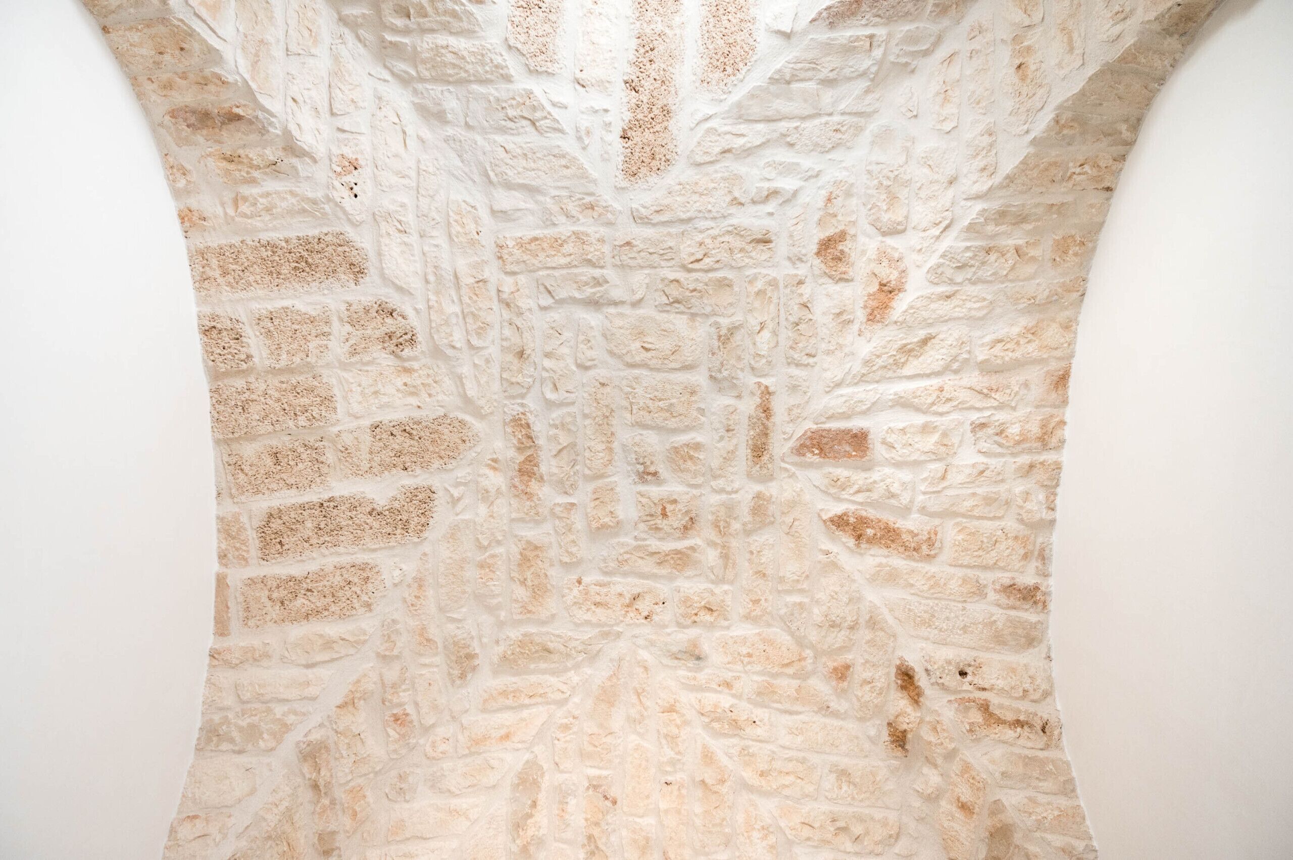 Un mur de pierre à la surface texturée, surmonté d’une arche incurvée.