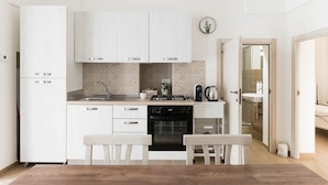 Una cucina compatta con mobili bianchi, lavastoviglie, fornello e lavandino. C'è un piccolo angolo ristoro con due sedie e una panca.