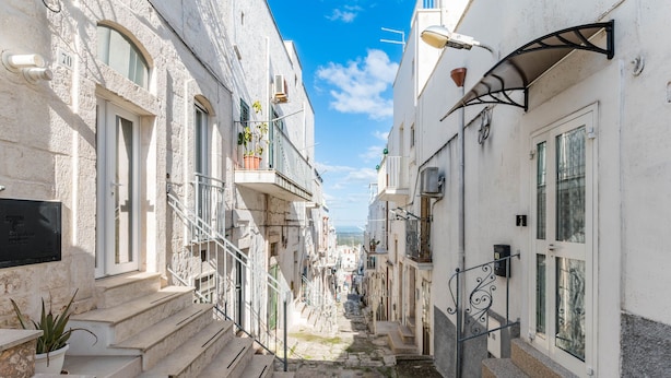Un vicolo stretto con edifici su entrambi i lati, gradini che portano all'ingresso e un cielo sereno.