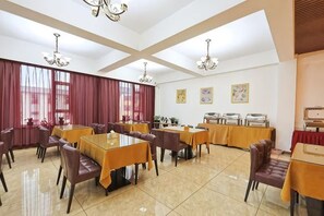 A hotel dining area with tables and chairs, a buffet setup, and a large window with curtains.