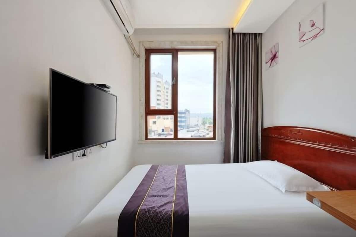Una habitación de hotel con cama, televisor, ventana y vista a la ciudad, y cabecero rojo.